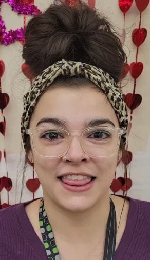 Photo of Savannah talking about how donated food helps her make ends meet. She has her hair in a tall bun, with Mardi Gras beads around her neck and a purple top.