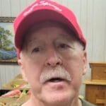 Photo of Bruce, an elderly gentleman who runs the food pantry, with a mustache and a red "Payne Springs" cap on his head.